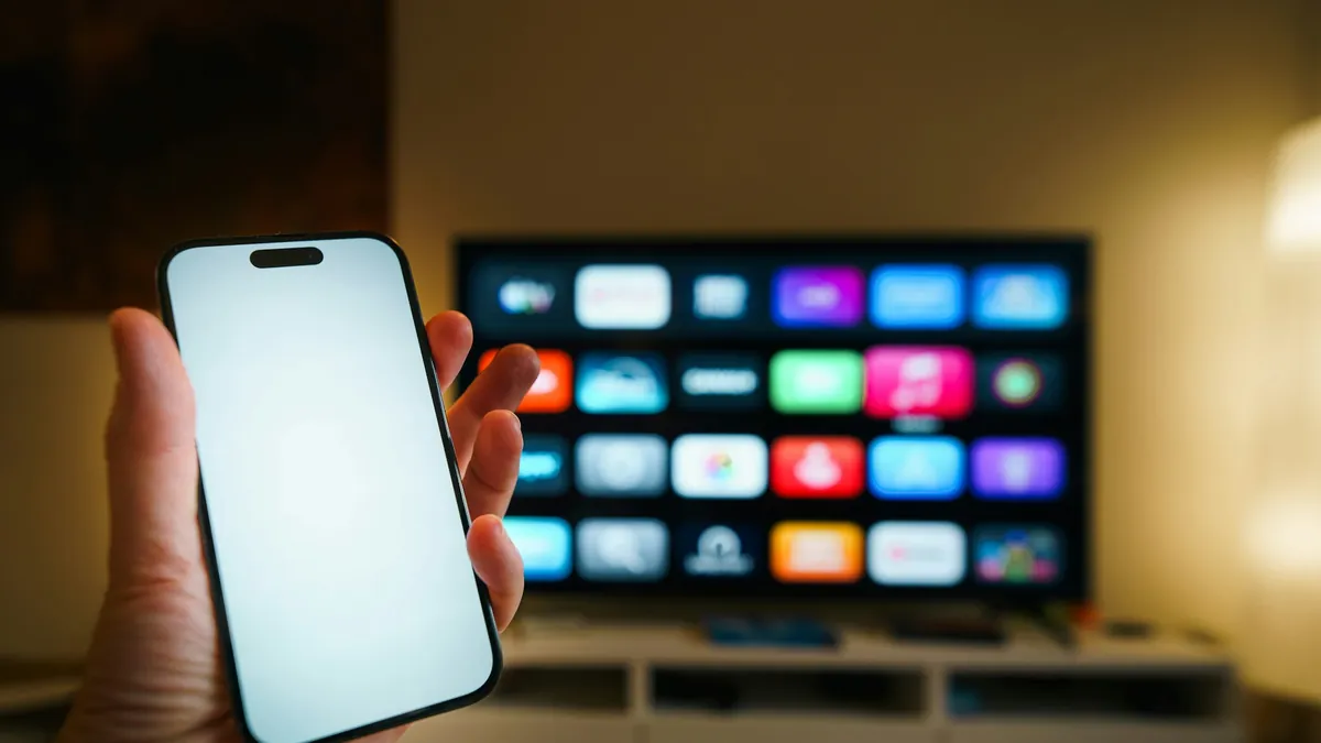 Phone held up in front of a smart TV, showing screen mirroring for IPTV on Roku