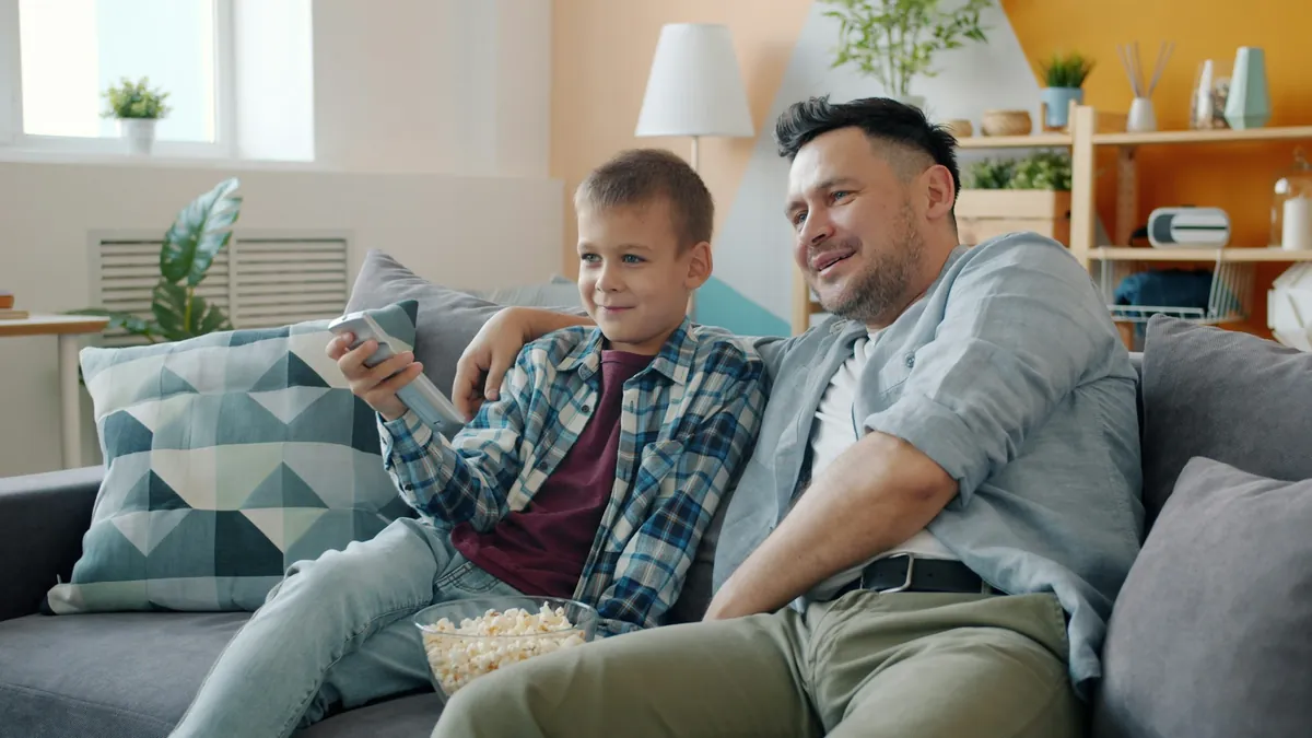 Father and son watching TV on the sofa, comparing IPTV with on-demand streaming apps
