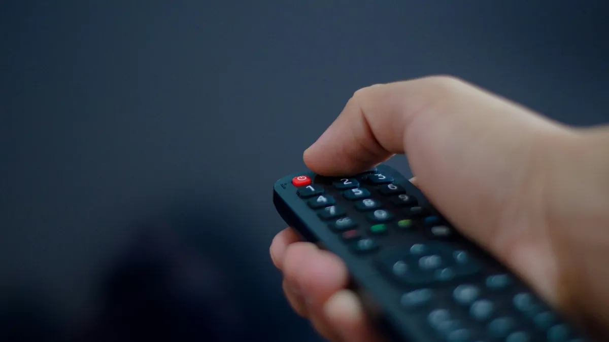 Hand holding a TV remote, ready to organise IPTV channels into favourites