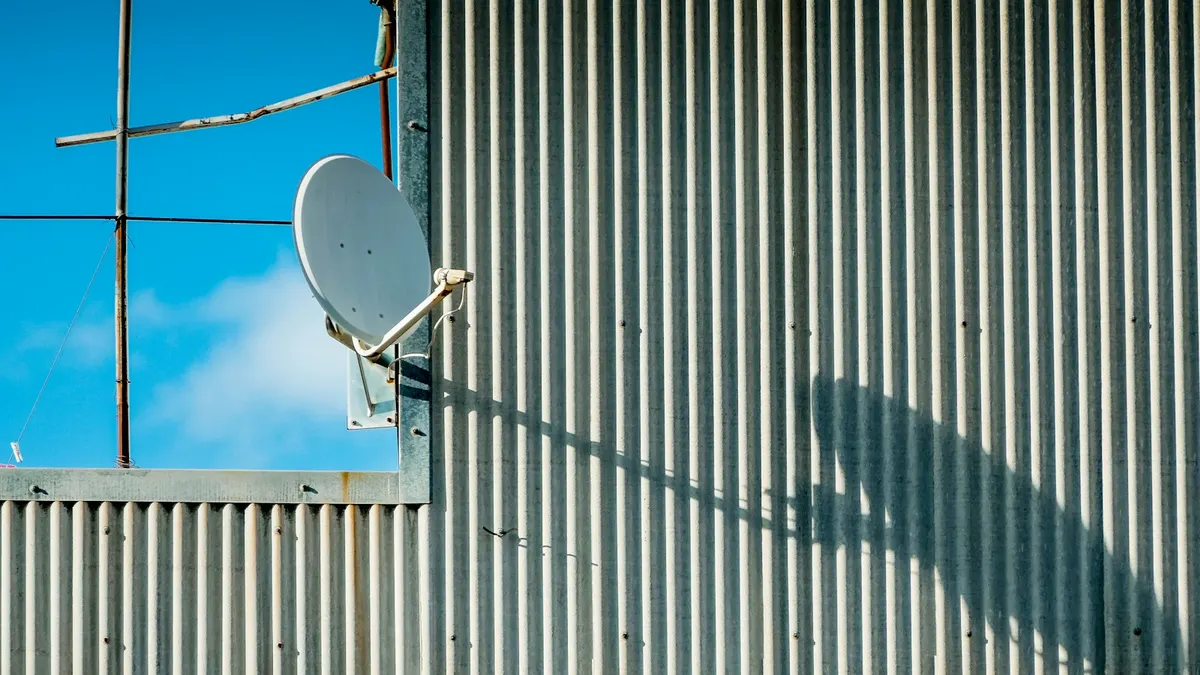 Satellite dish on a corrugated iron wall, one way to get a Sky Sport subscription in NZ